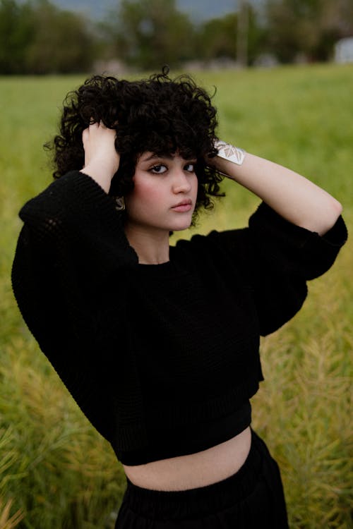 A woman with curly hair is posing in a field