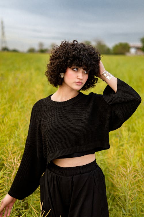 A woman with curly hair is standing in a field