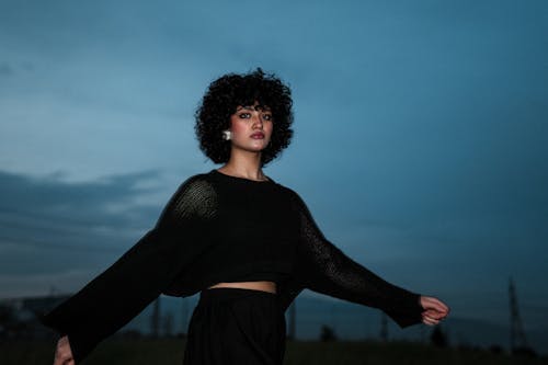 A woman with curly hair and a black top standing in the field