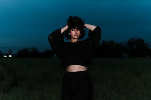 A woman in a black crop top and skirt standing in a field