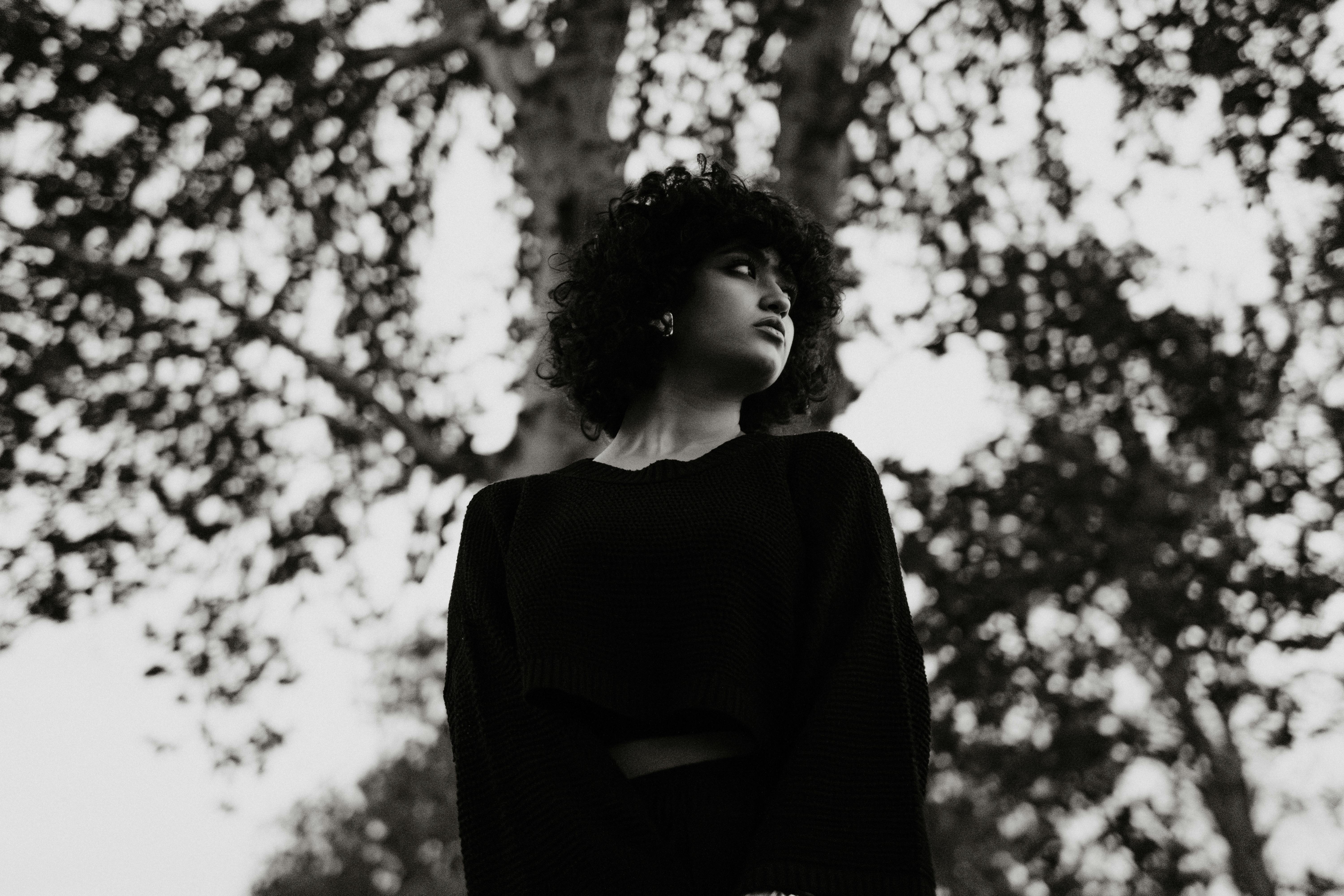 Striking black and white portrait of a woman with curly hair set against trees.