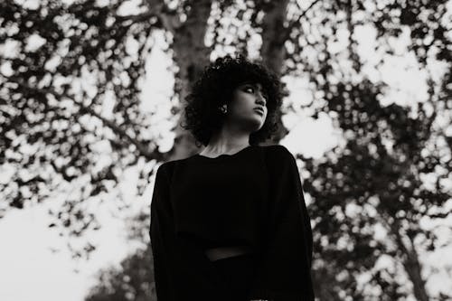 A woman with curly hair standing in front of trees