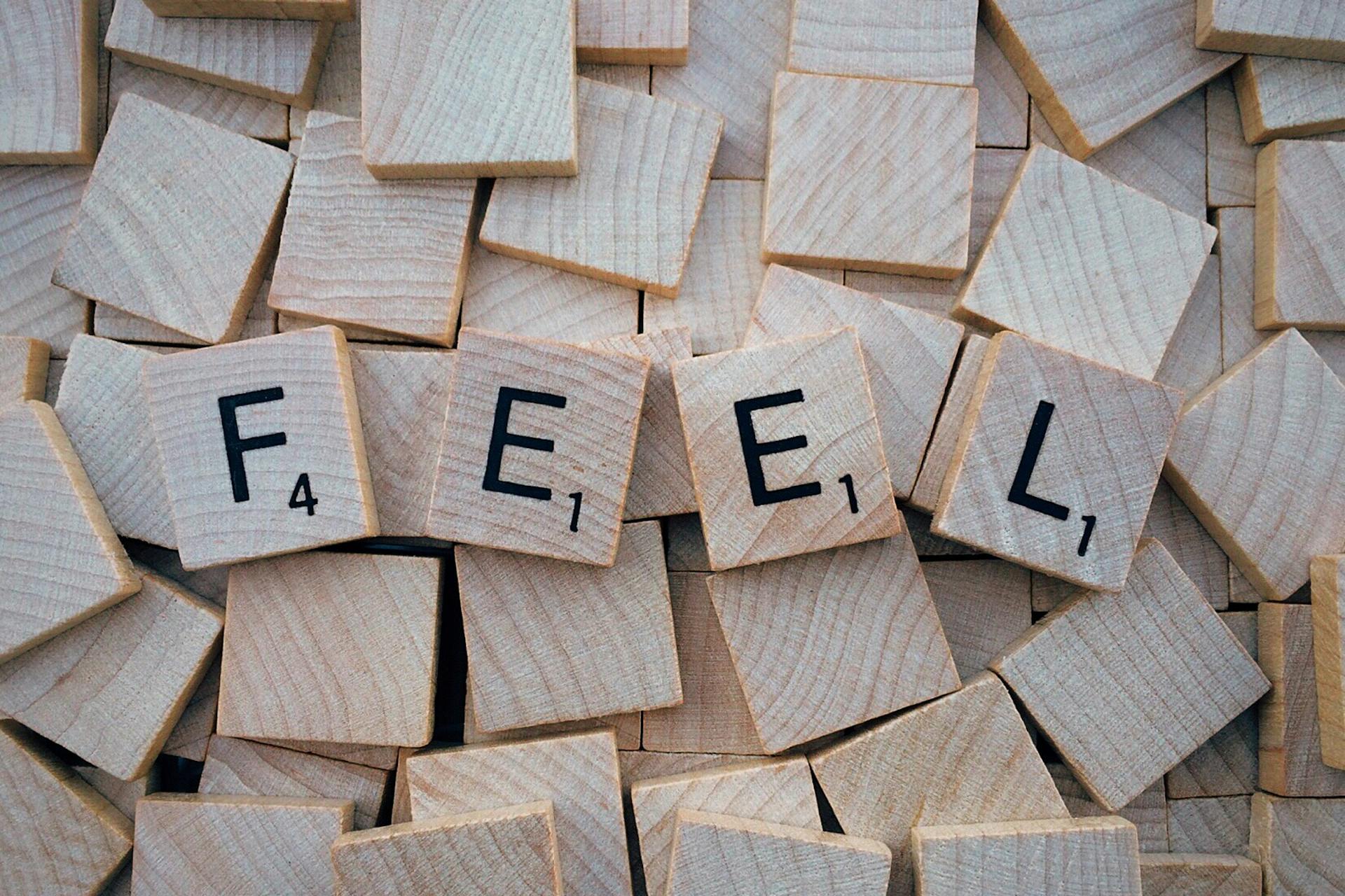 Close-up of Scrabble tiles spelling 'Feel' scattered on a wooden background.