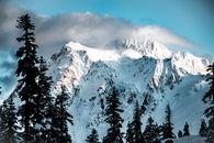冬日晴朗的天空下，白雪覆盖的山峰与针叶树构成壮丽景色
