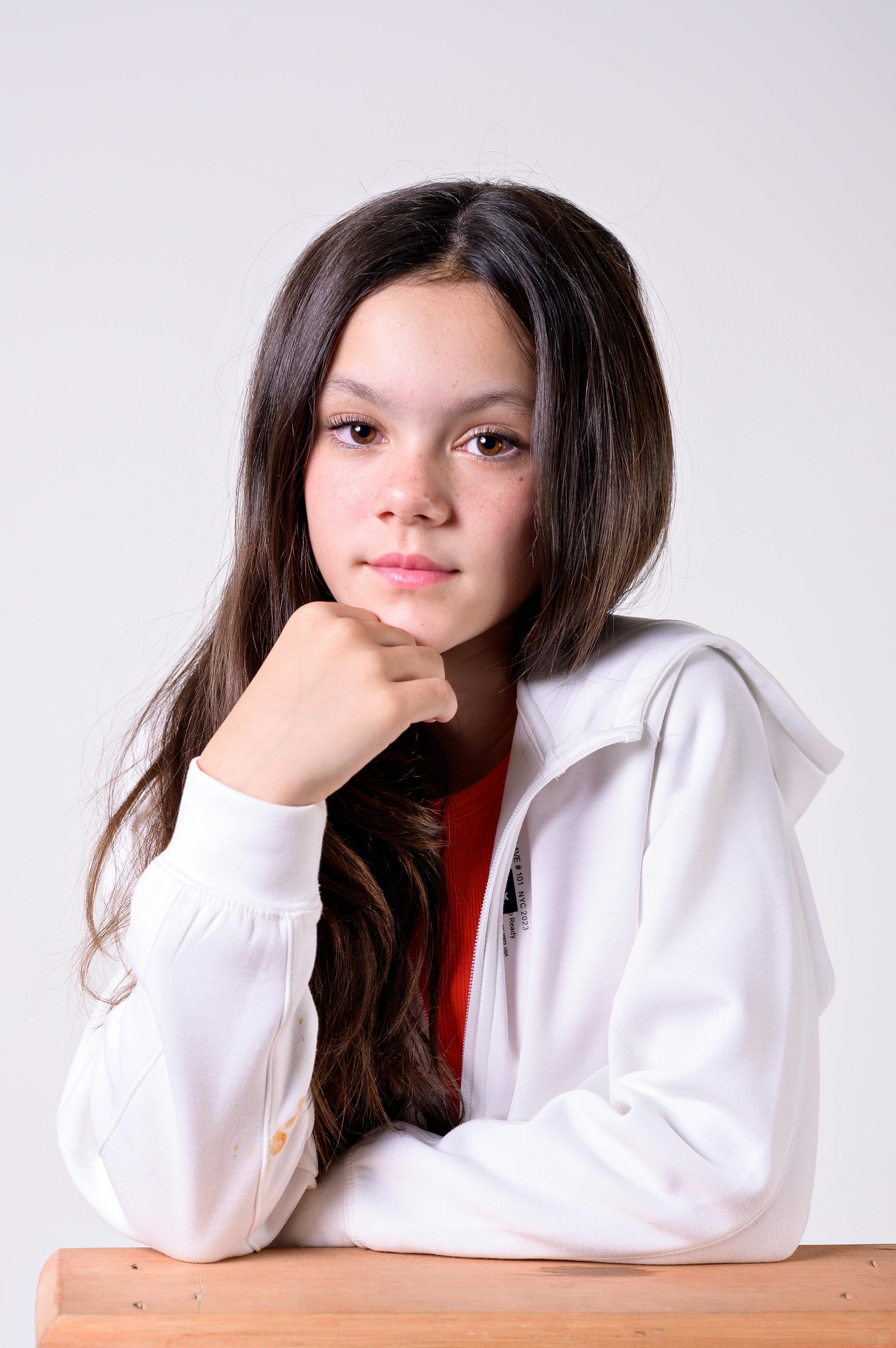 Portrait of a teenage girl in a white hoodie with long hair, looking thoughtful.