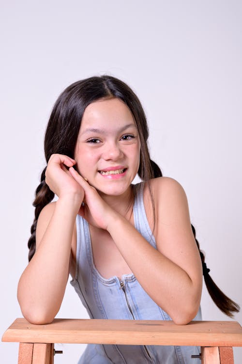 A young girl sitting on a stool with her hair in braids