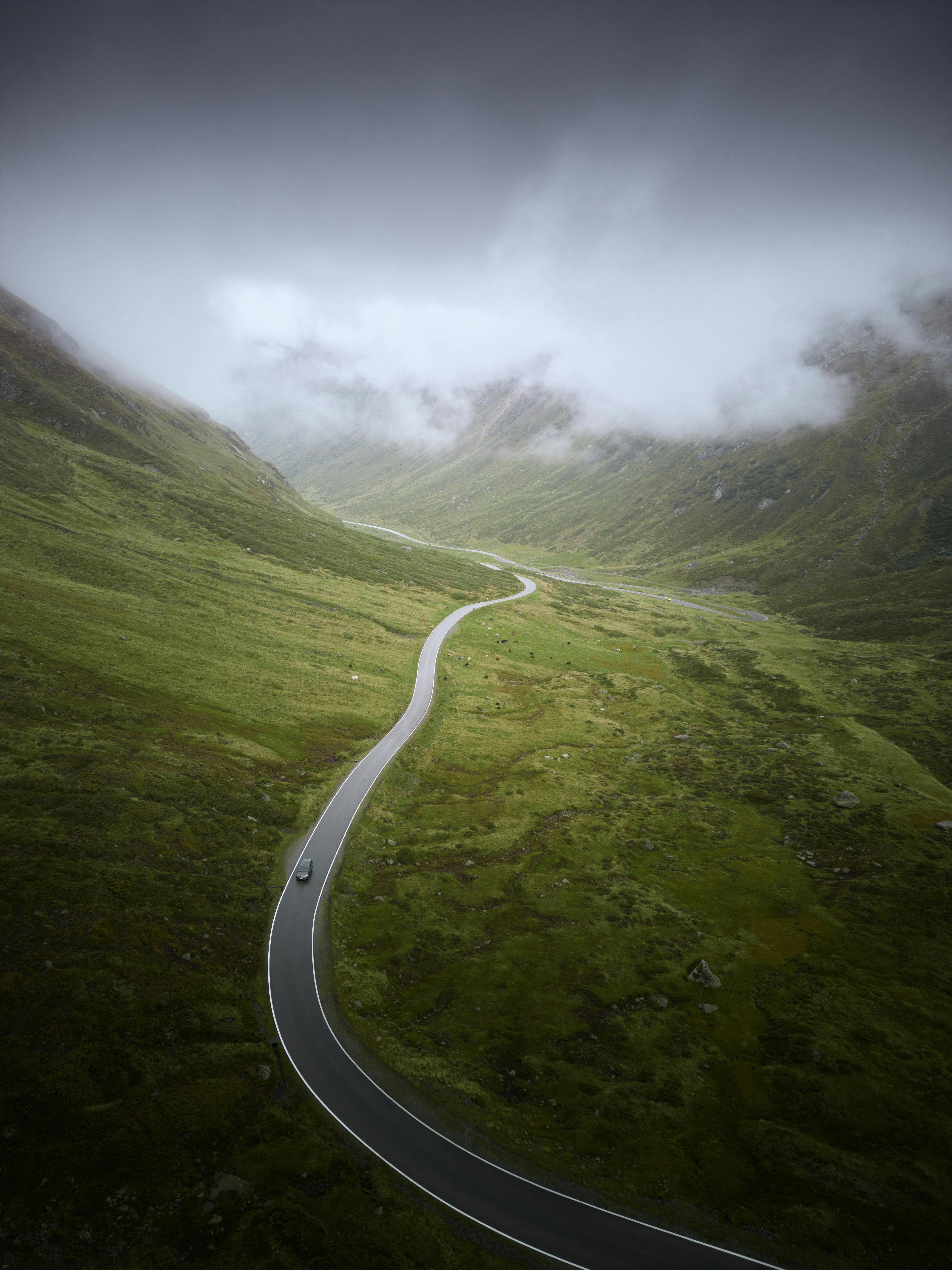 Scenic aerial view of a winding road through misty green hills and mountains with fog, ideal for travel and nature themes.