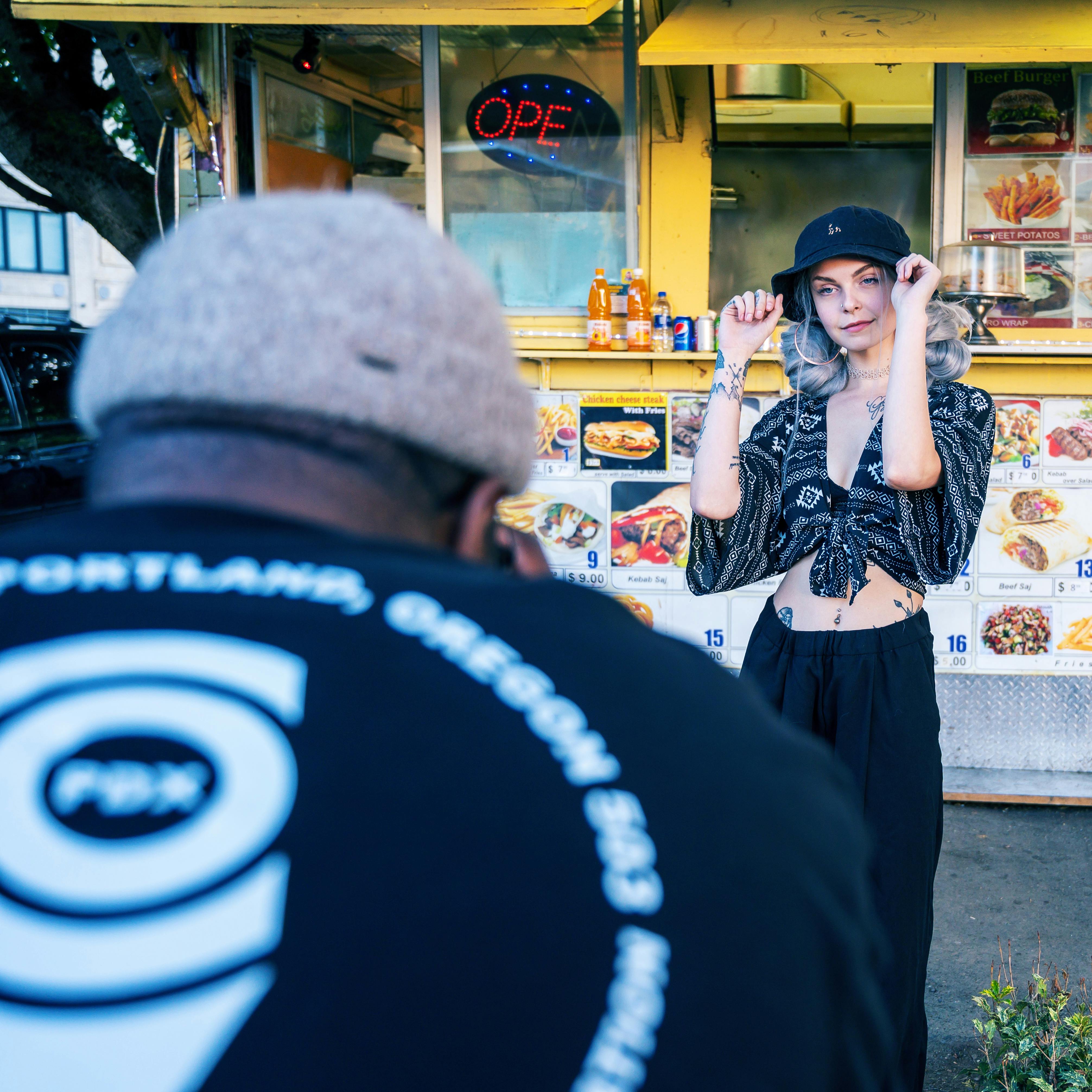 A fashion model poses stylishly in front of a vibrant food truck during a street photoshoot.