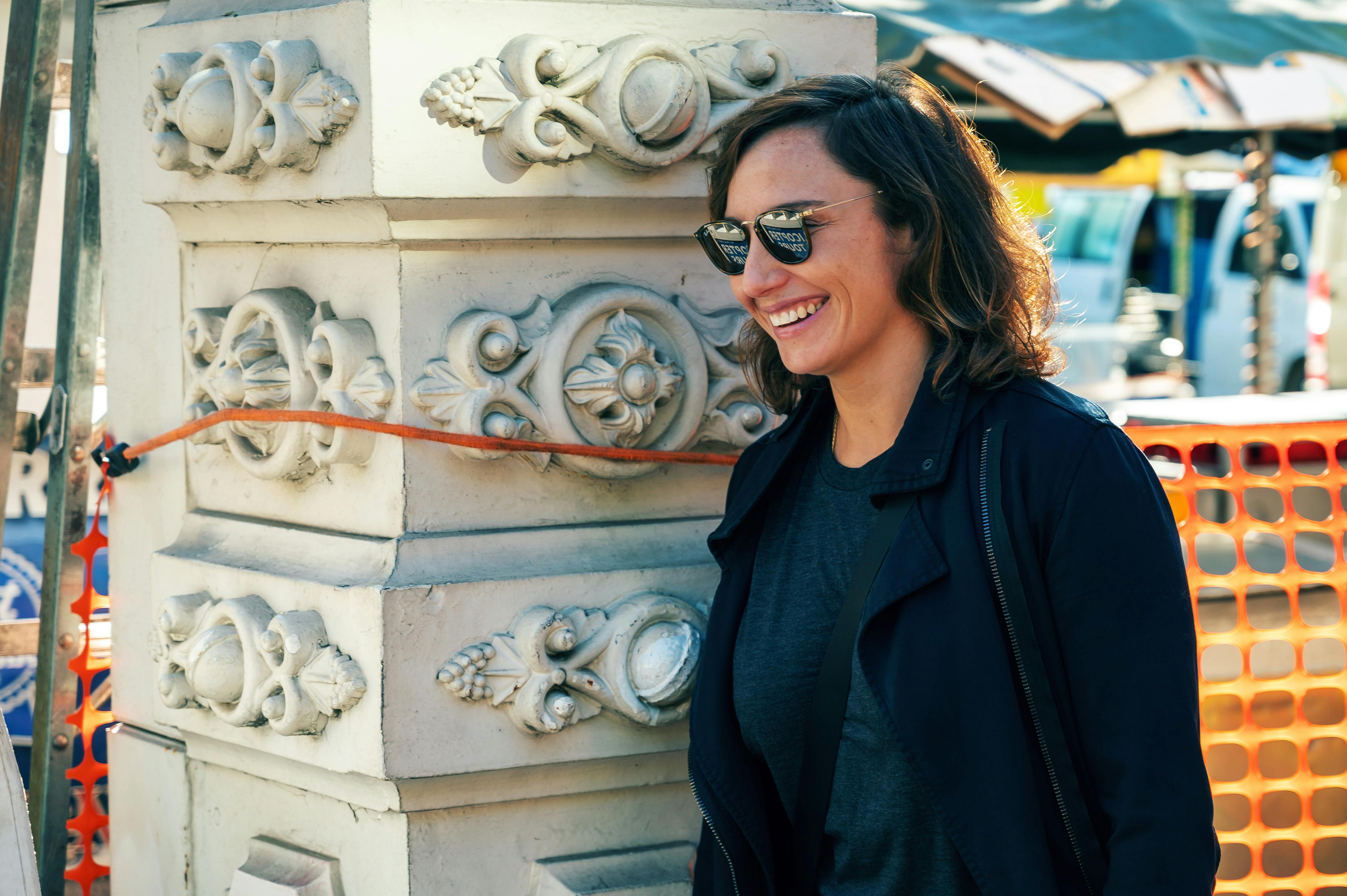 A fashionable woman smiles in an urban environment with decorative architecture.