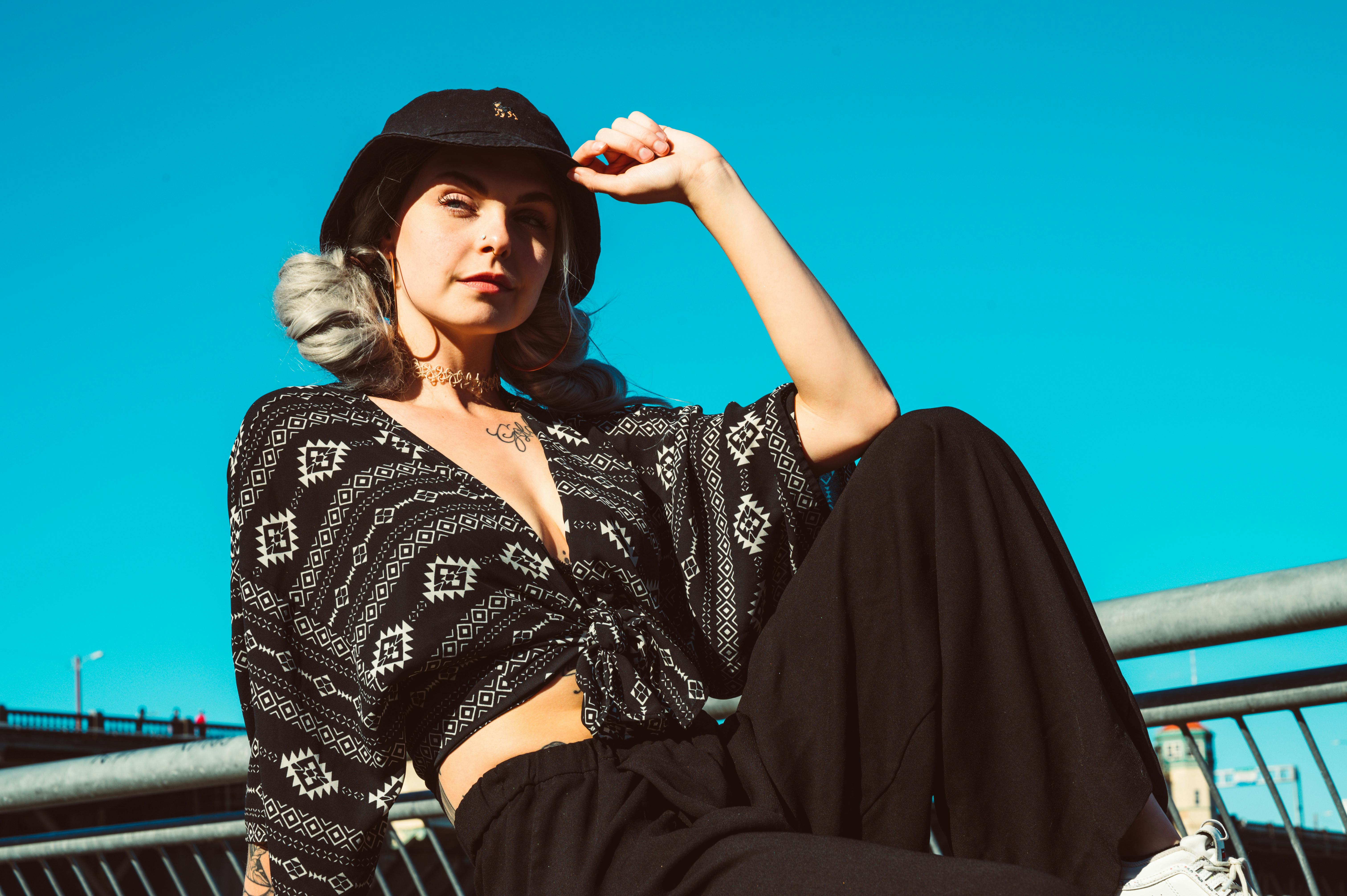 Young woman in stylish outfit posing outdoors with sunlight illuminating her against a clear blue sky.