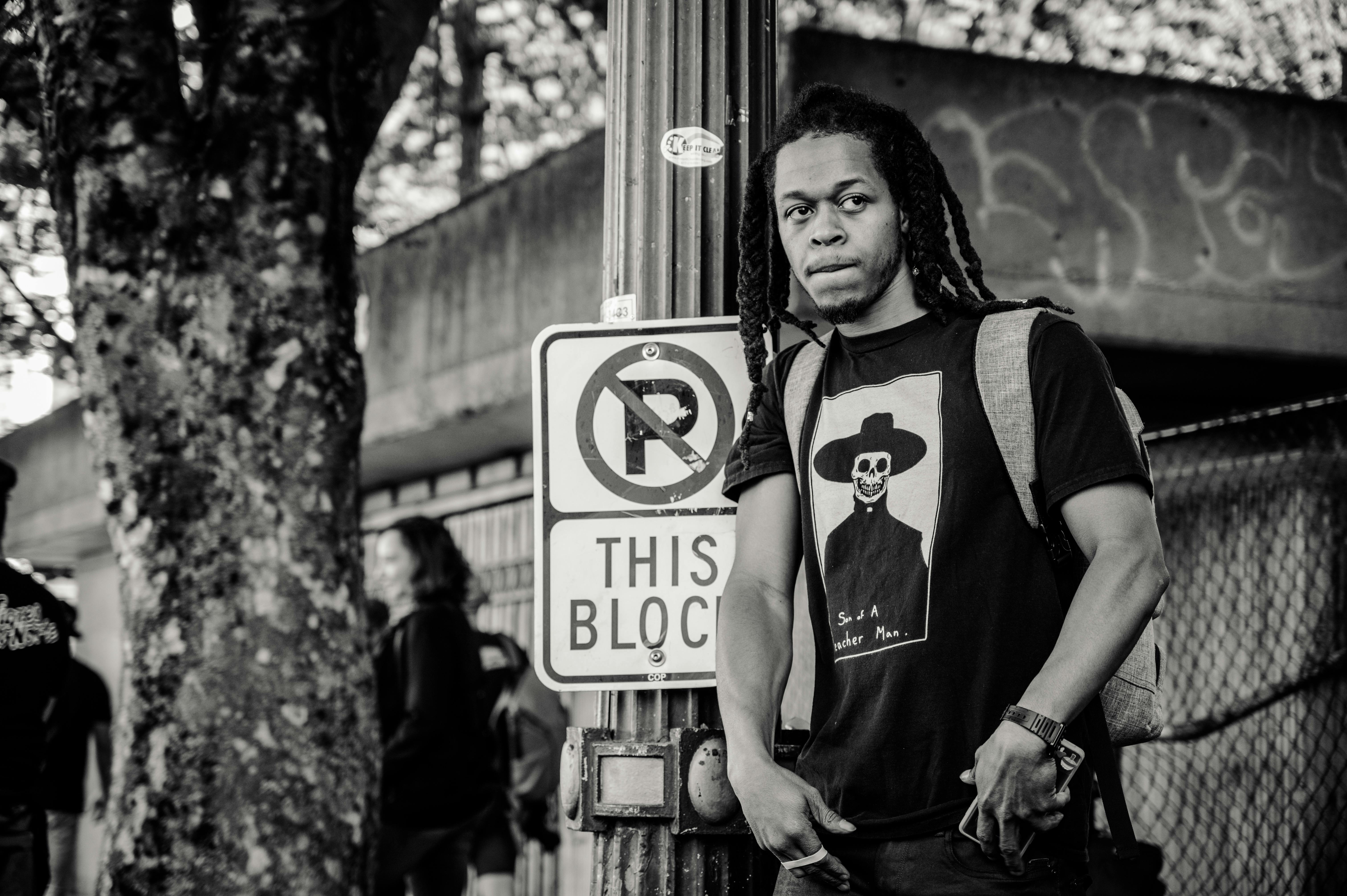 Black and white portrait of a man standing next to a no parking sign in a city street.