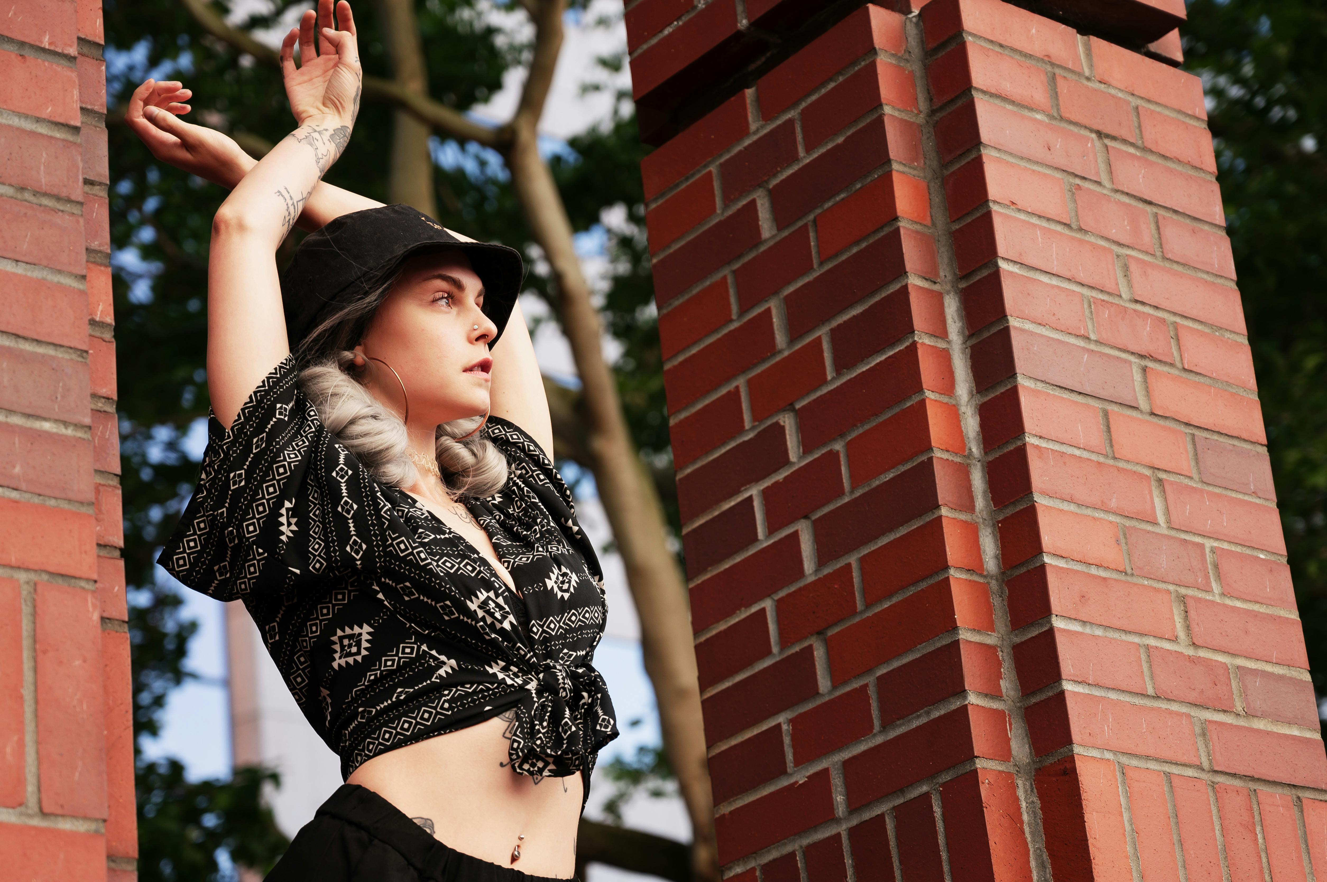Free Stylish woman in black outfit posing elegantly beside brick columns outdoors. Stock Photo