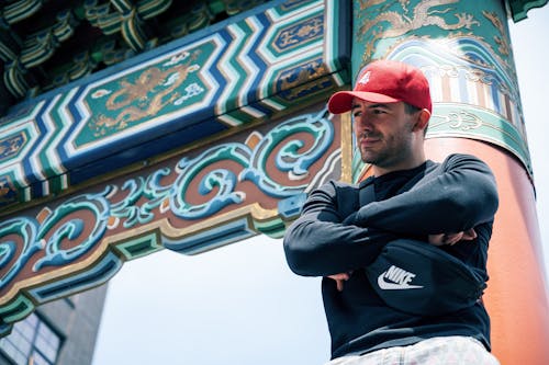 Foto De ángulo Bajo Del Hombre Apoyado En El Pilar Chino Rojo Posando Con Los Brazos Cruzados Mirando Hacia Otro Lado