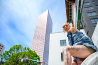 在城市环境中，一名身着牛仔布纹身的女子在高耸的摩天大楼前摆出姿势，采用低角度拍摄