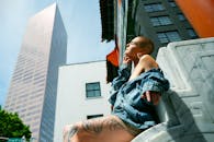 一位身着牛仔夹克的女人，正以高耸的摩天大楼为背景，在户外晒太阳