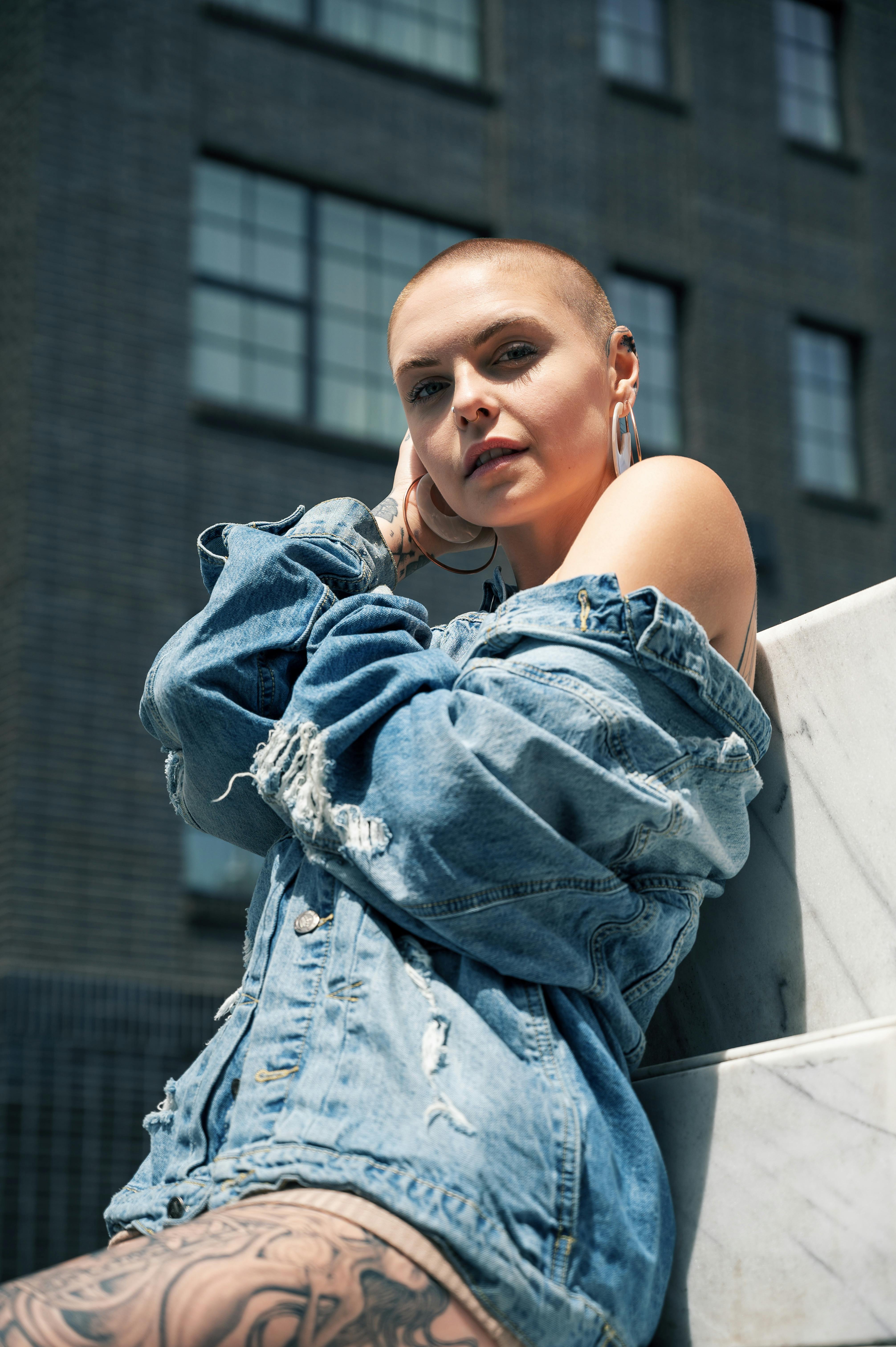 Bold fashion-forward woman with short hair and tattoos posing in an urban setting.