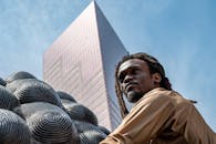 在现代摩天大楼的背景下，一座雕塑摆出长着辫子的男人的肖像姿势