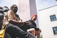 两名男子坐在城市建筑背景下的户外雕塑上