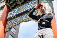 一位戴着帽子的男子在传统的中式大门下摆姿势，色彩鲜艳夺目