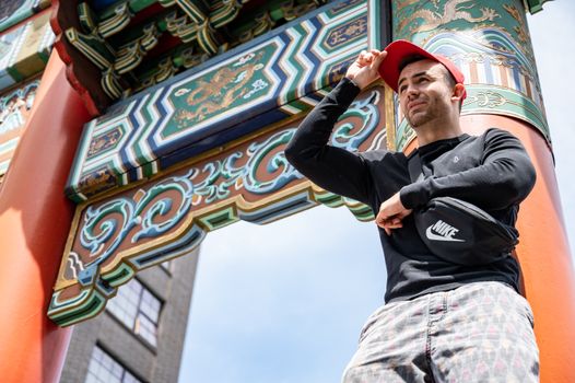 一位戴着帽子的男子在传统的中式大门下摆姿势，色彩鲜艳夺目