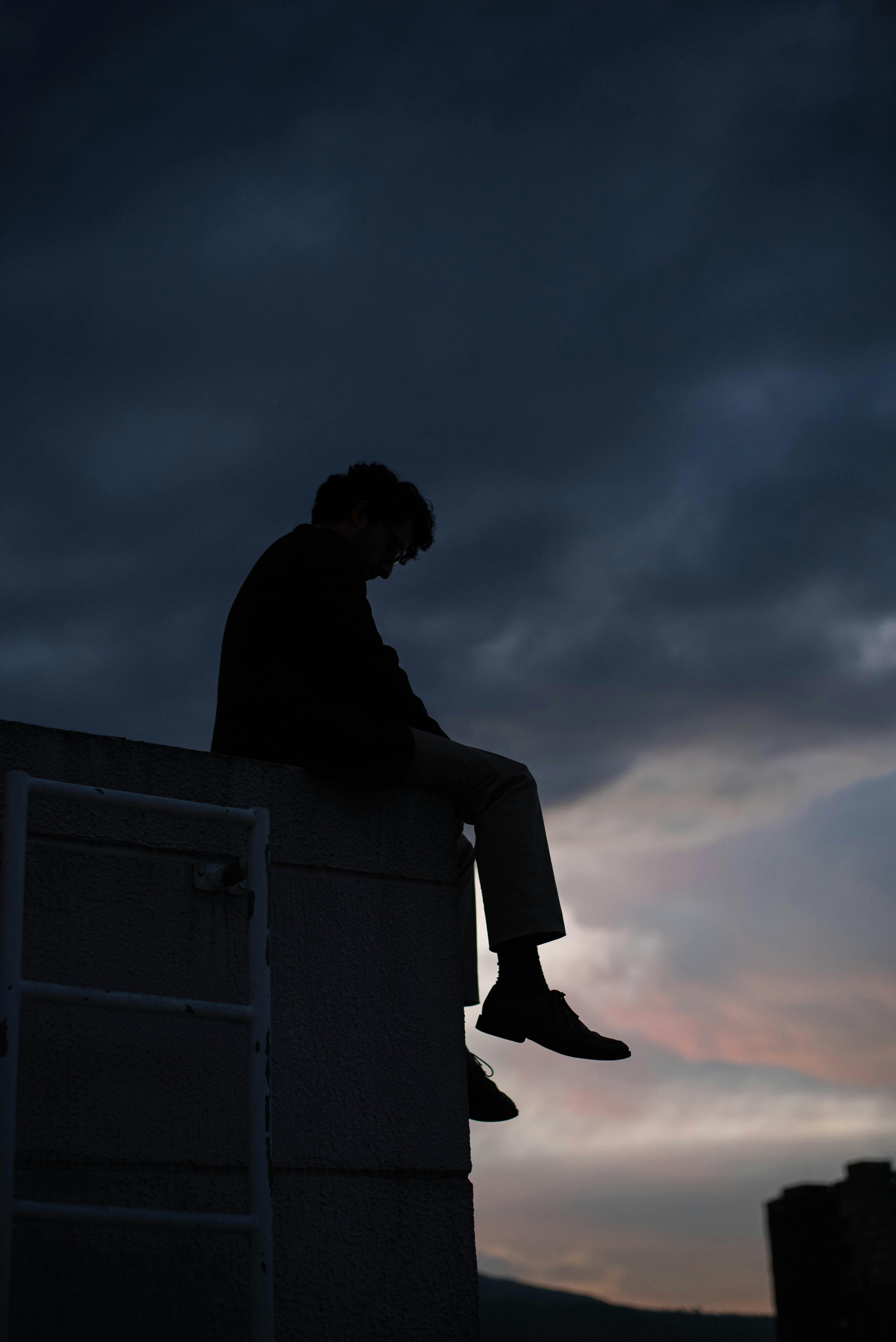 Silhouetted person sitting on a rooftop against a dramatic twilight sky.