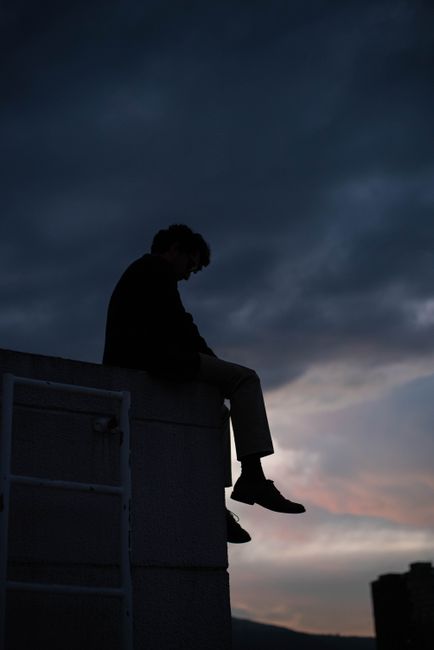 Silhouetted person sitting on a rooftop against a dramatic twilight sky.