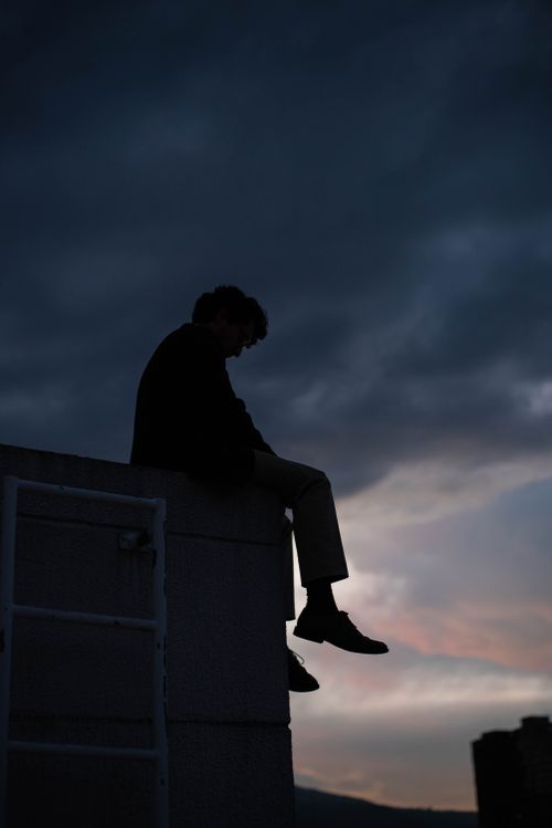 Free Silhouetted person sitting on a rooftop against a dramatic twilight sky. Stock Photo