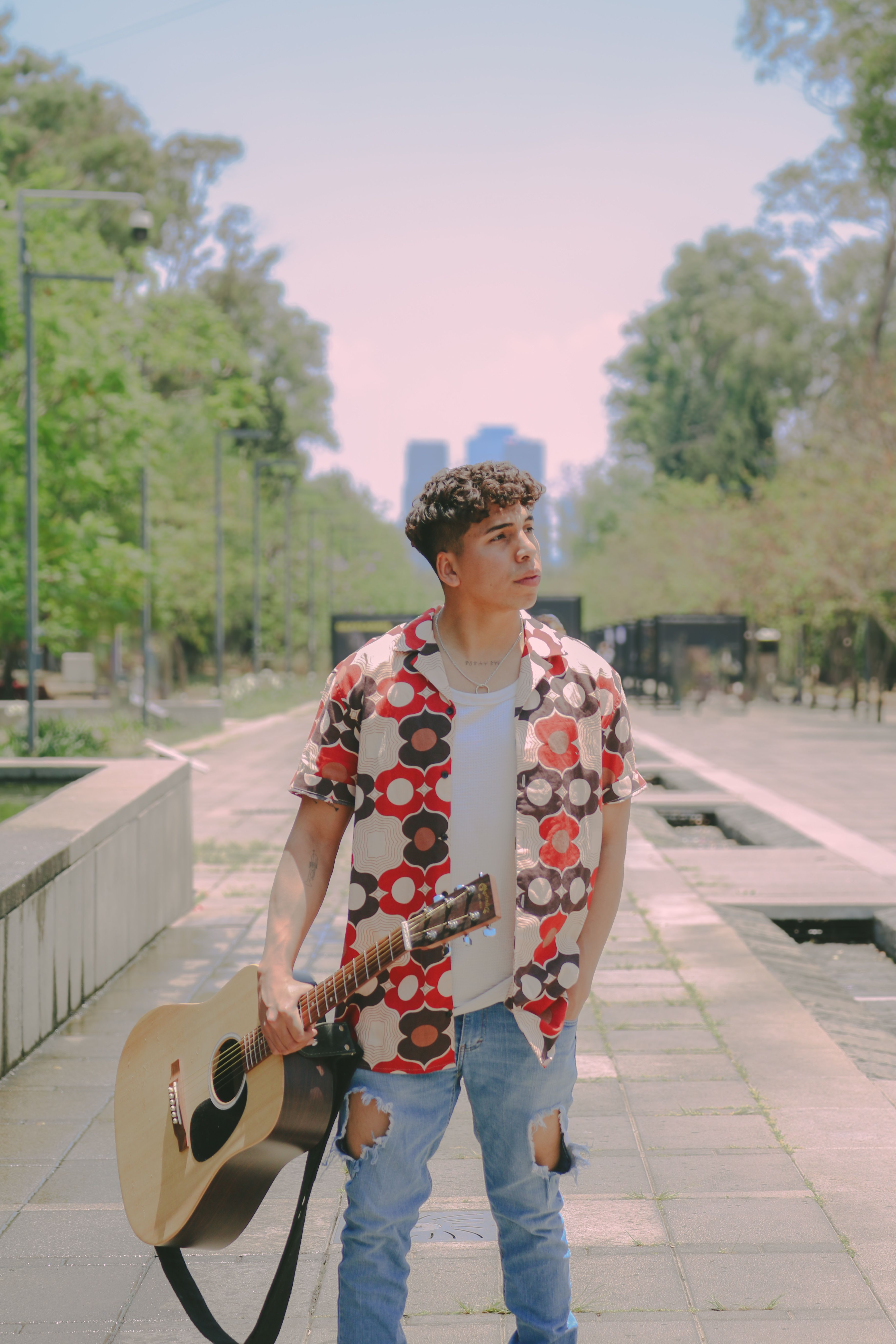 Young musician with guitar outdoors in an urban park setting, a perfect blend of music and nature.