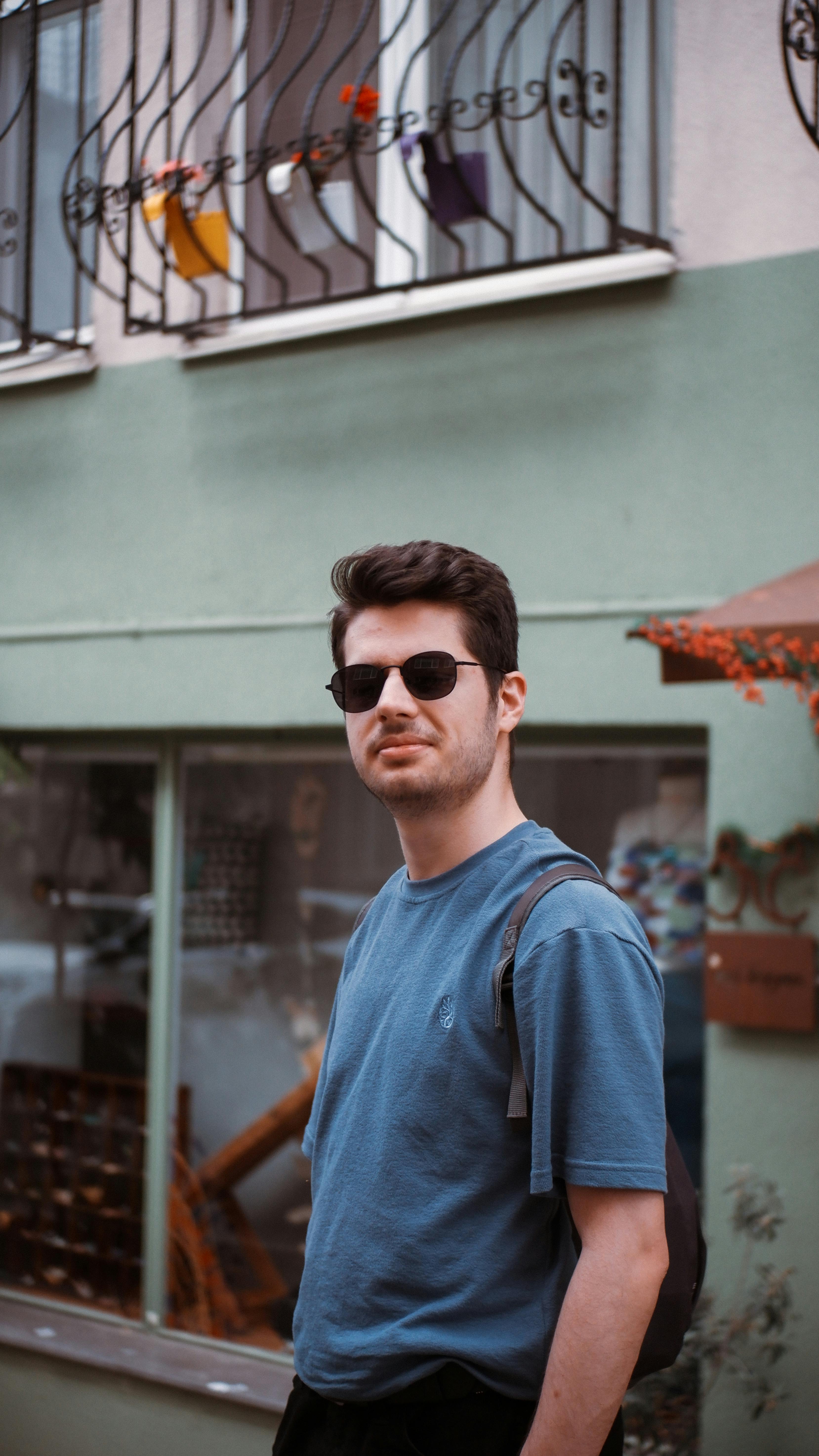 Portrait of a man in a blue t-shirt and sunglasses, with a casual urban backdrop.