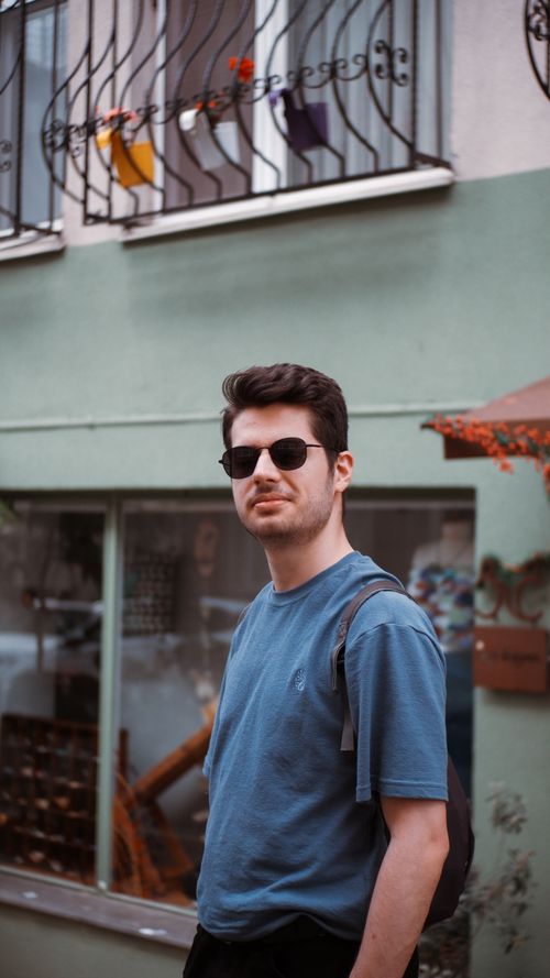 Free Portrait of a man in a blue t-shirt and sunglasses, with a casual urban backdrop. Stock Photo