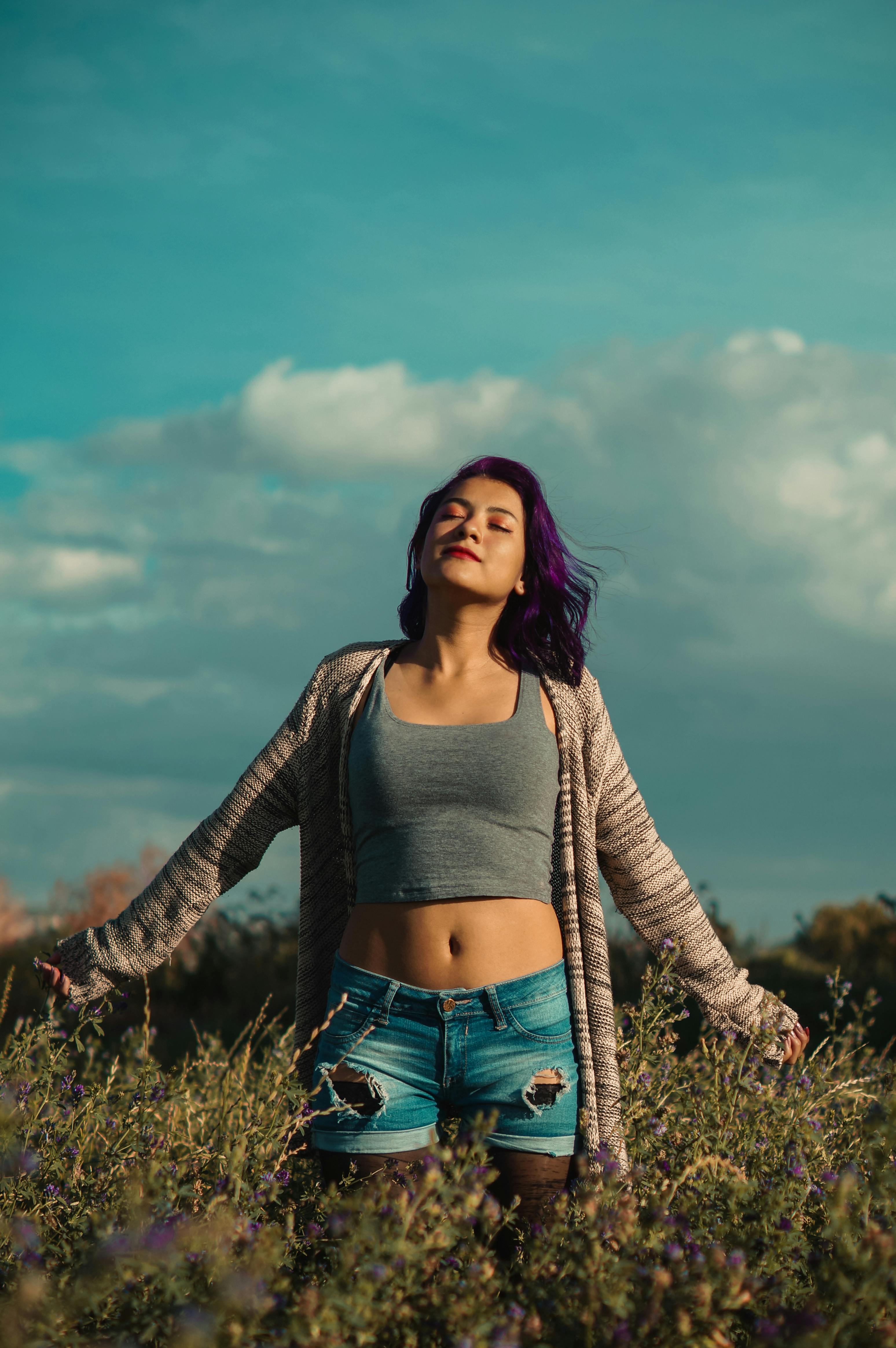 一位紫发年轻女子在绿野中，享受着阳光明媚的一天，拥抱大自然