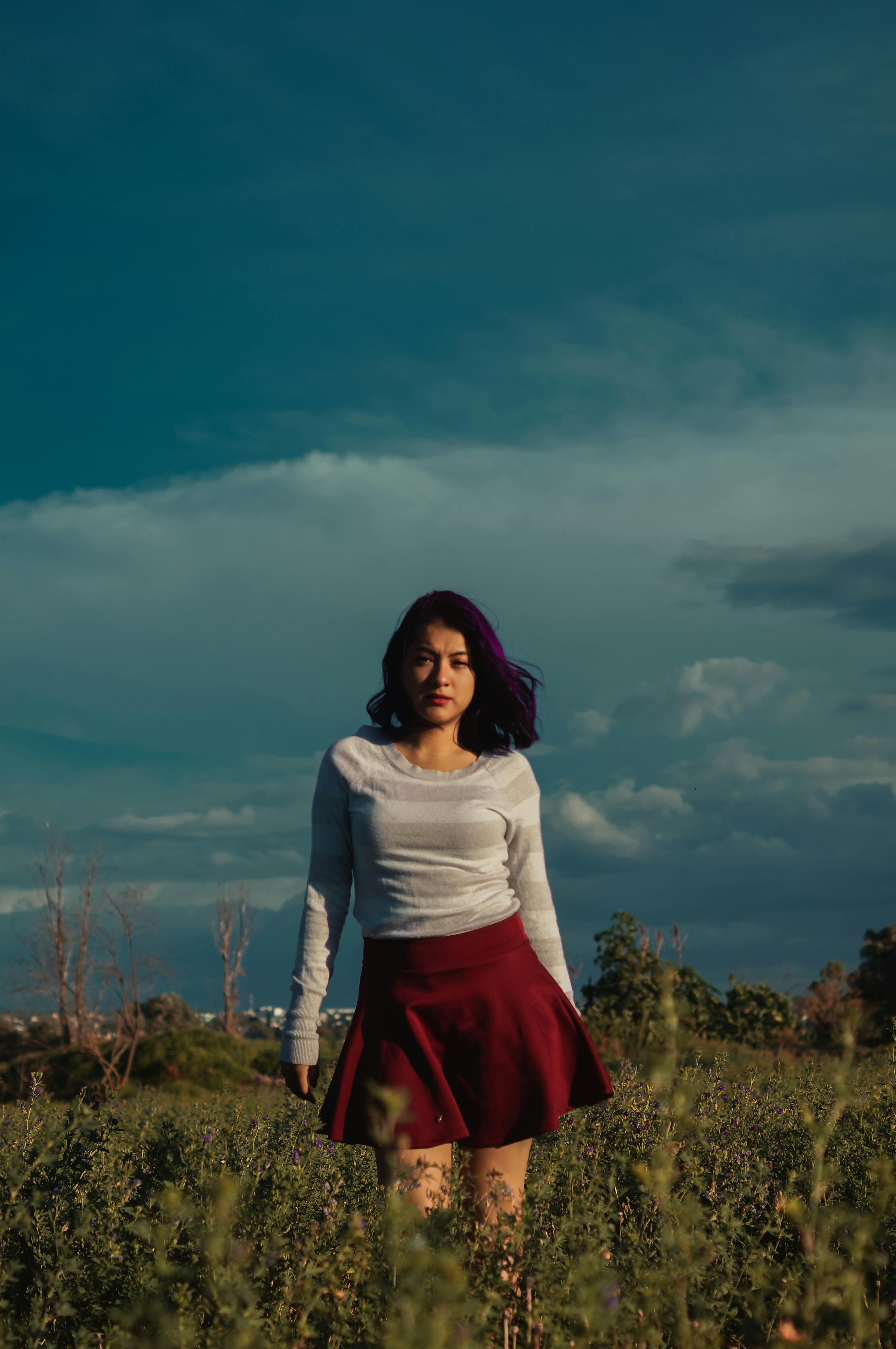 woman standing on grass field under white clouds and blue sky