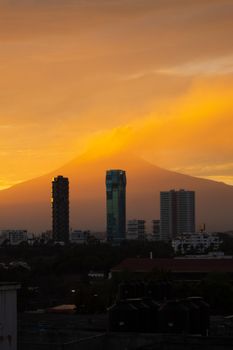 Dramatic sunset over Puebla city skyline with Popocatépetl volcano in the background, creating a stunning natural scene.