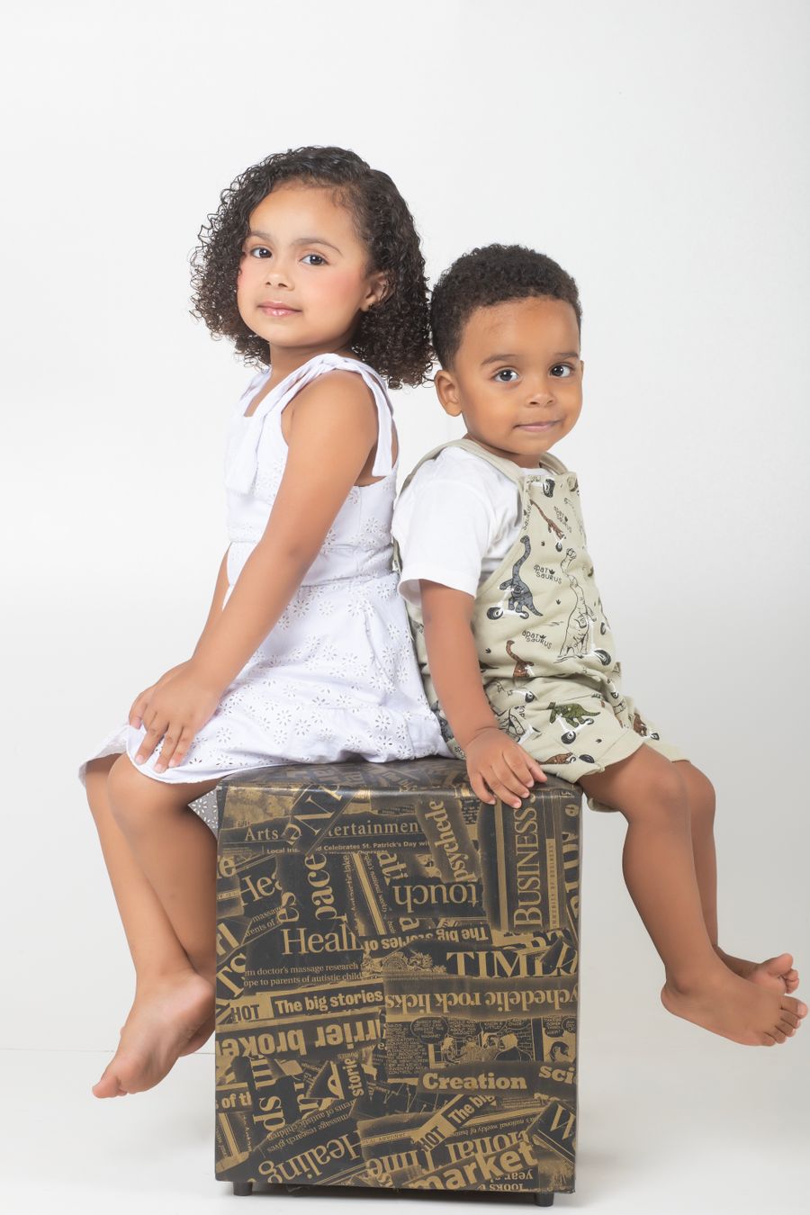 Two siblings sitting back to back on a studio box