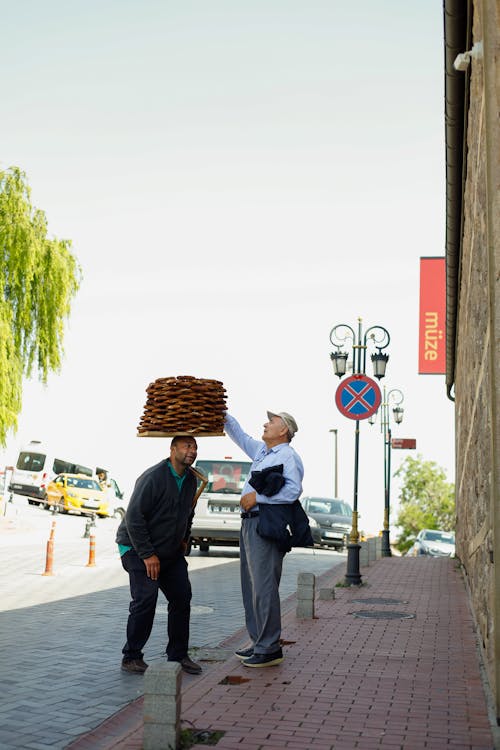 Two men are carrying a large stack of bread on the sidewalk