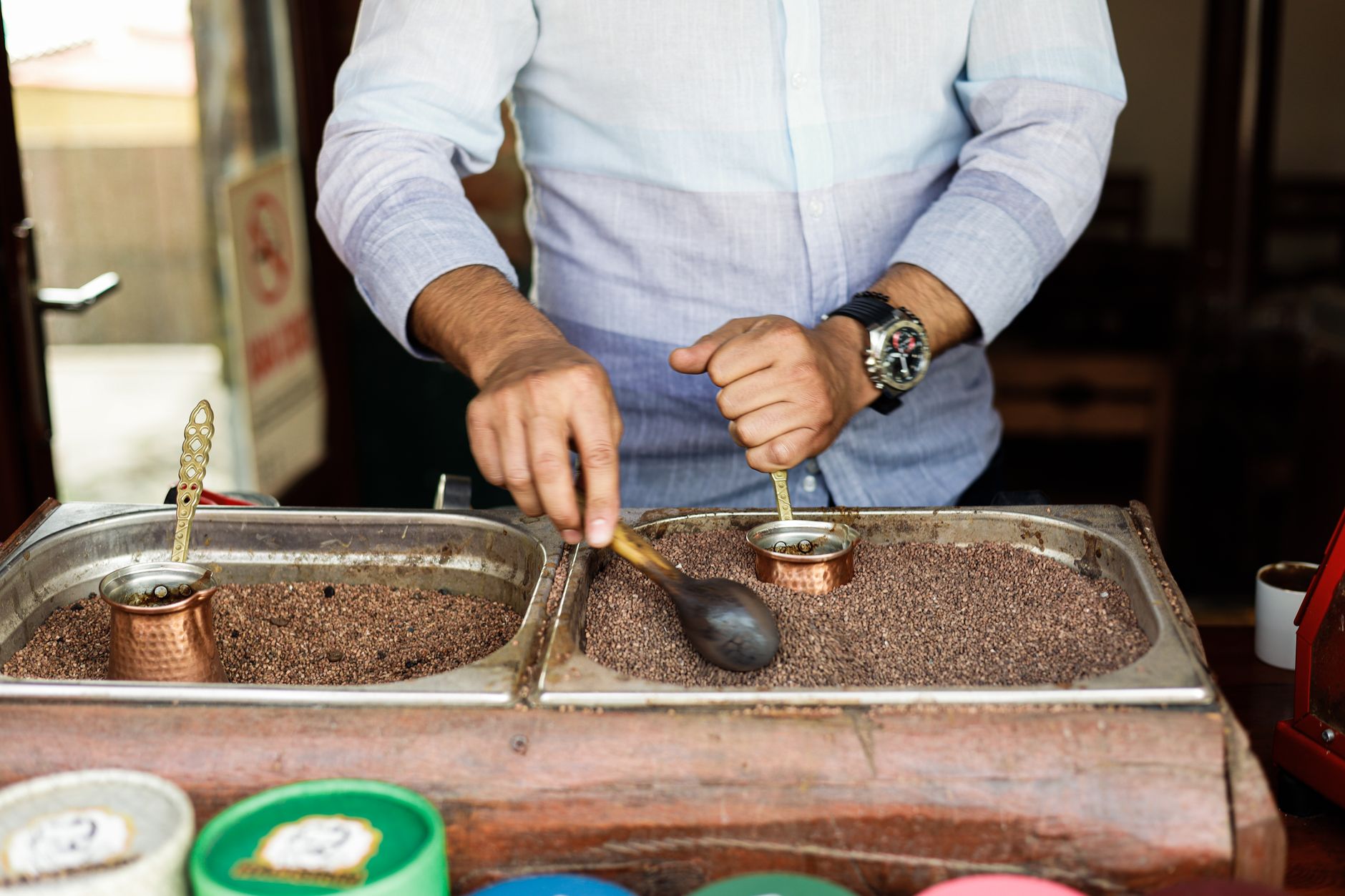 Man preparing traditional Turkish coffee using copper pots in a café setting.