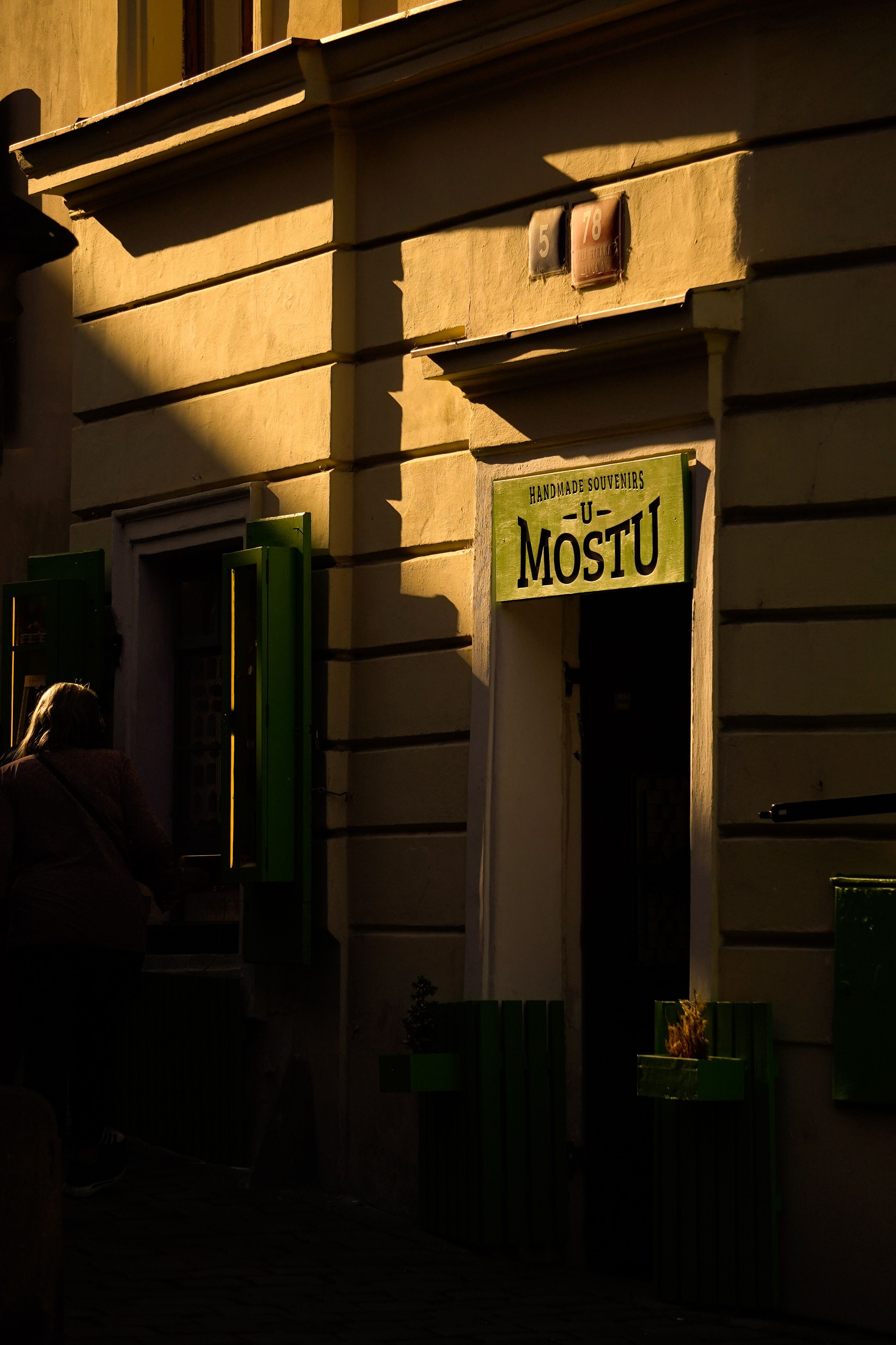 Shadowed building entrance with green accents and a unique sign, captured in warm evening light.