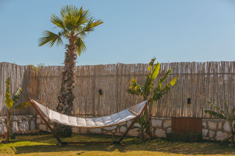 A relaxing hammock in a sunny tropical backyard with palm trees and a blue sky.