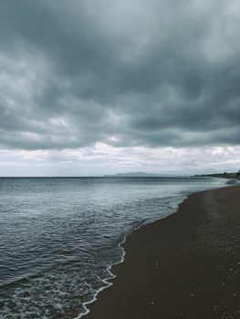 A serene beach with dark clouds and calm sea, capturing an overcast day by the shoreline.