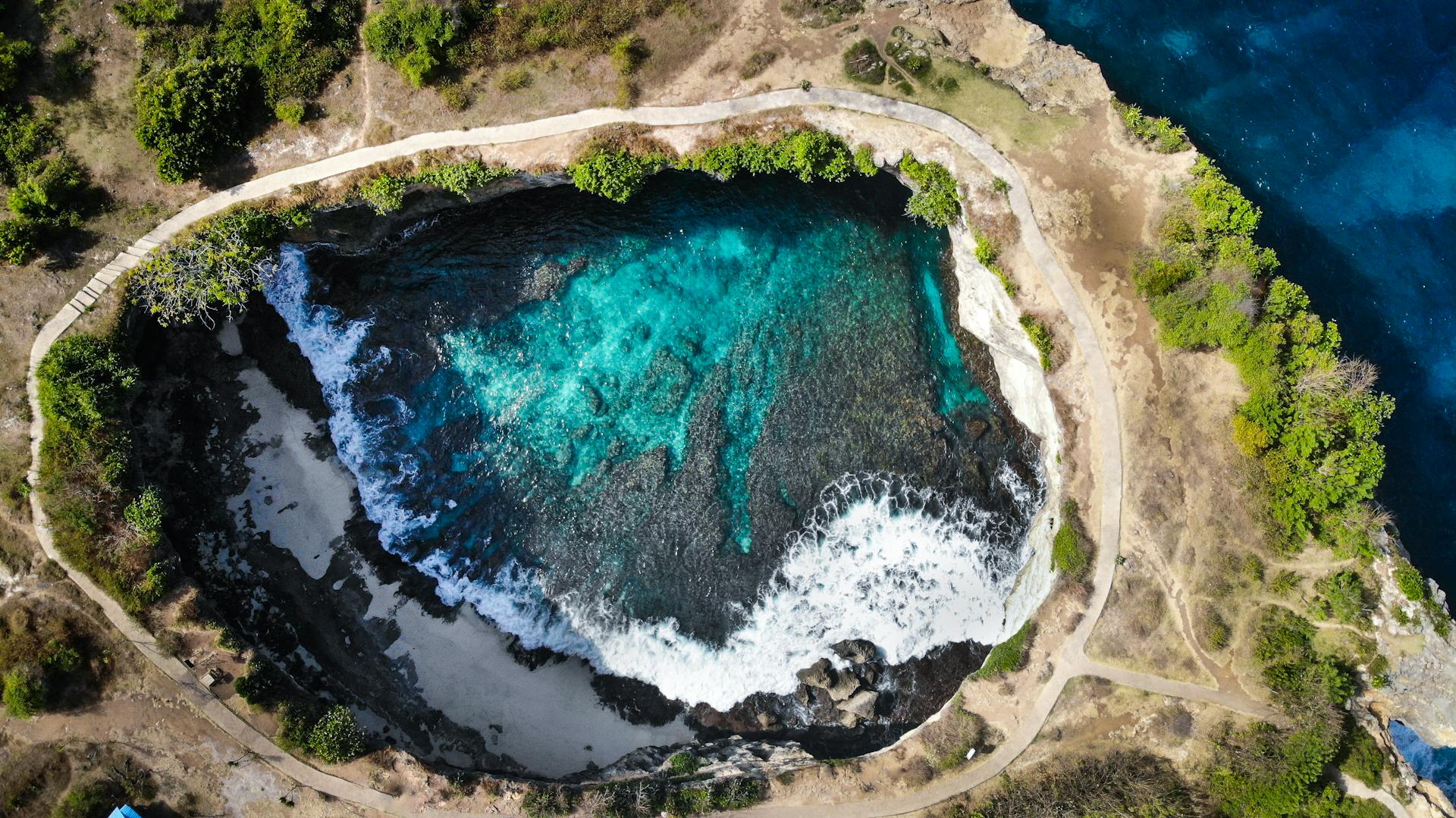 Stunning aerial view of Angel's Billabong in Bali showing turquoise waters and rocky cliffs.