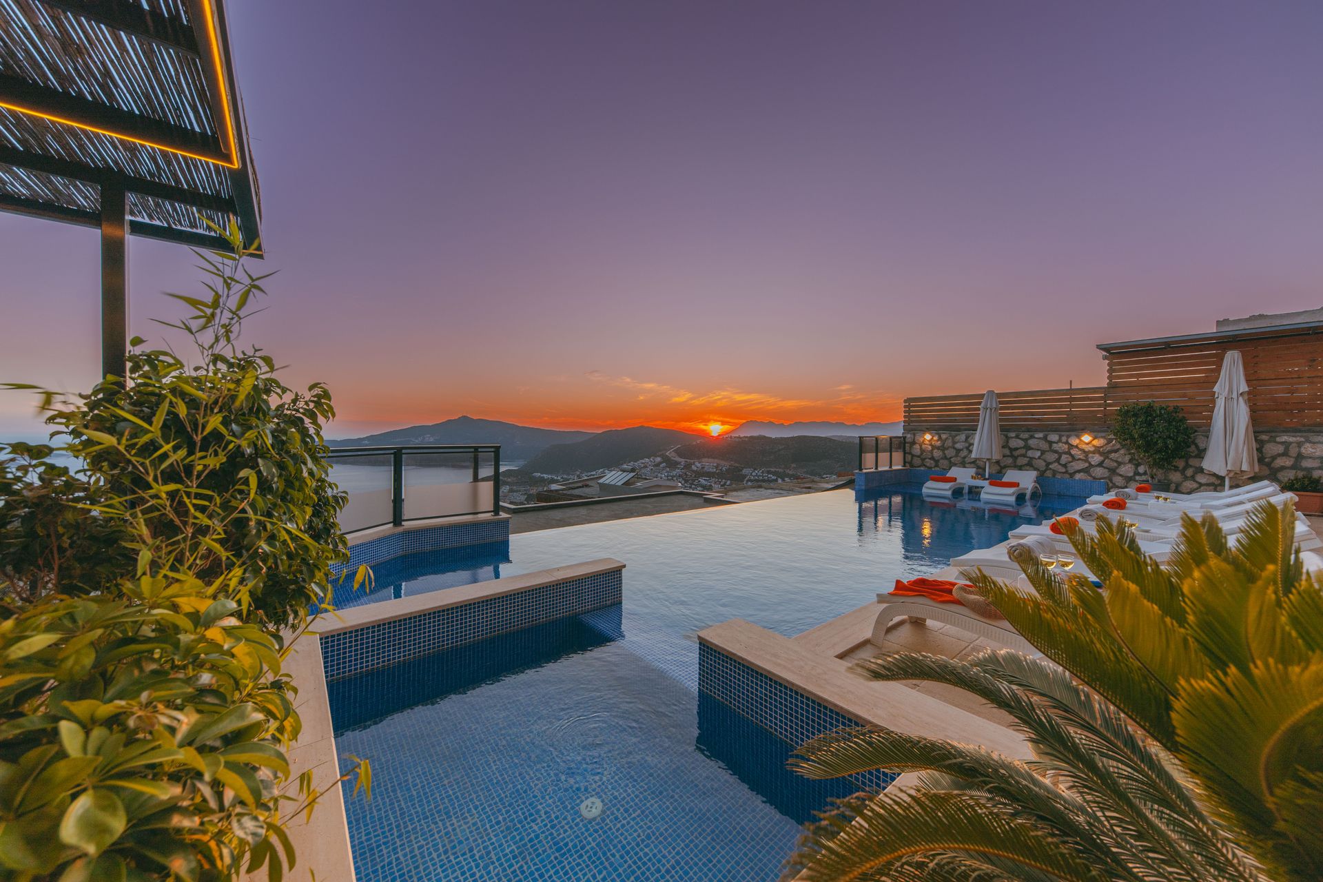 Infinity pool overlooking the coast at sunset, lounge chairs along the water's edge