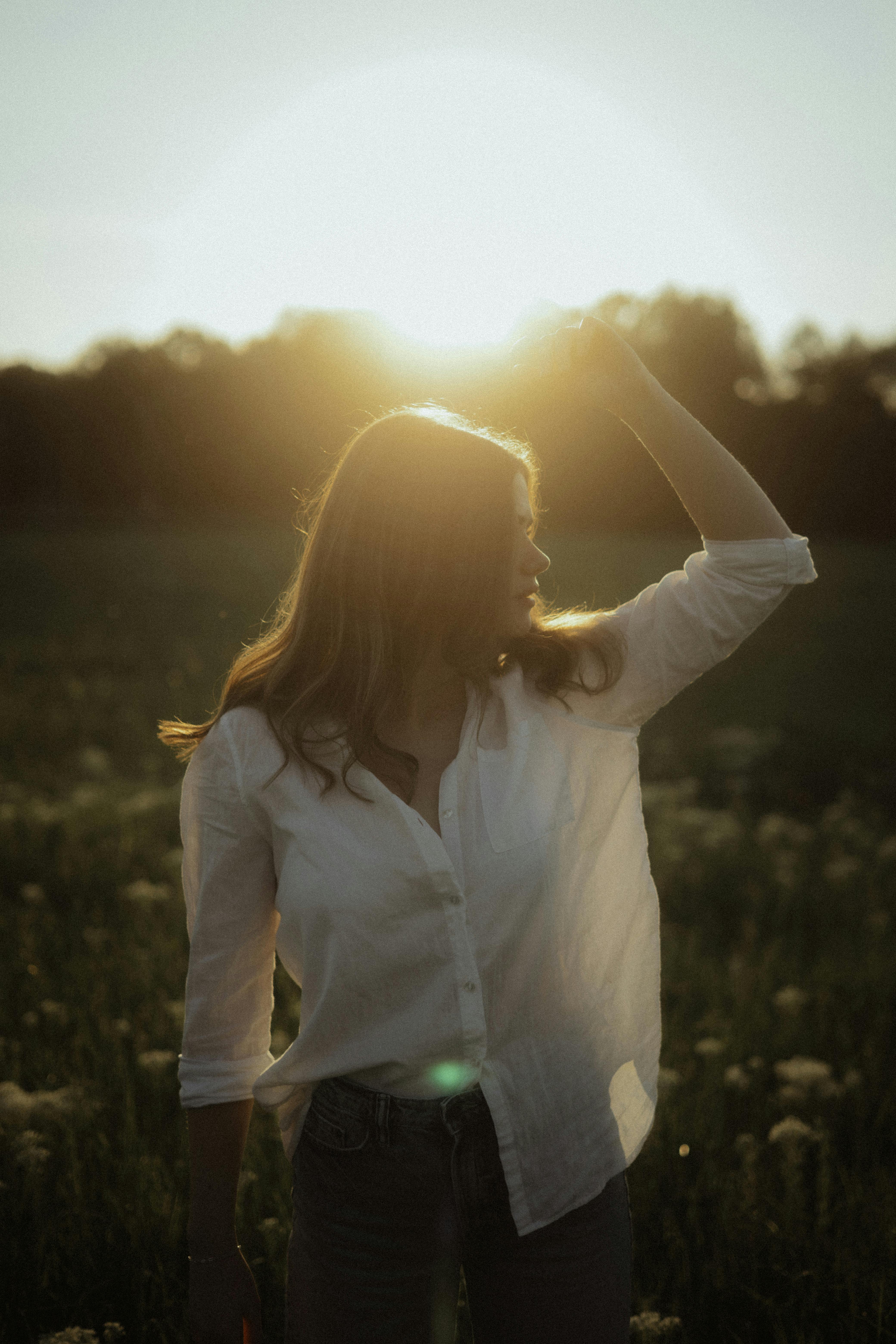 Woman standing in meadow during sunset, backlit for dramatic effect.