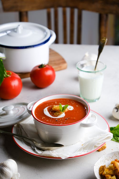 A bowl of tomato soup with bread and a spoon