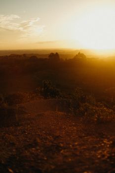 A serene golden sunset casting a warm glow over rolling hills with trees and soft earth.