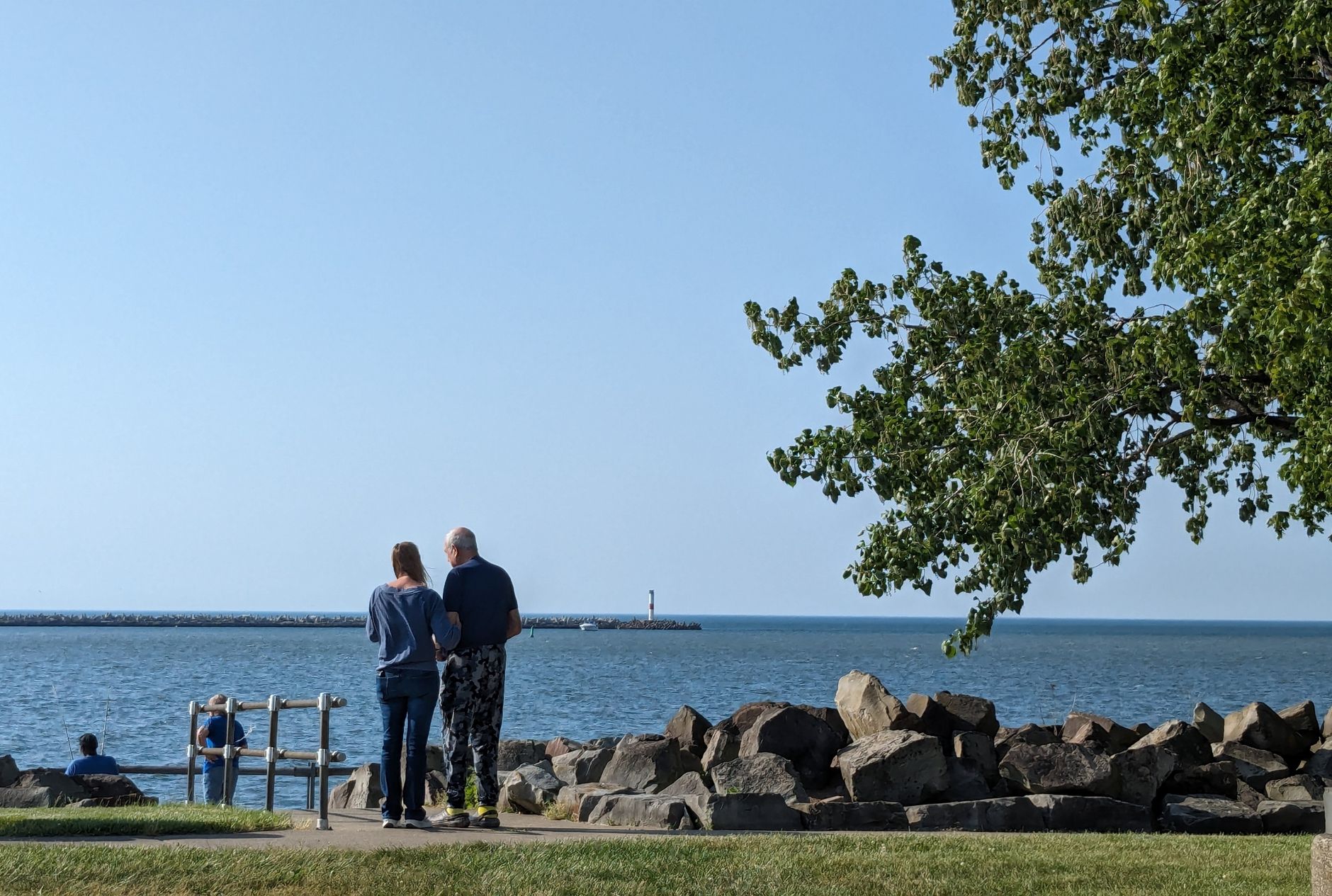 Couple standing near rocks by the sea, enjoying a peaceful summer day at the coast.