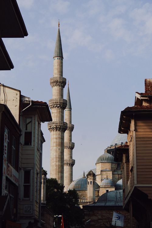 Free A picturesque view of an historic mosque with towering minarets framed by urban buildings, under a clear sky. Stock Photo