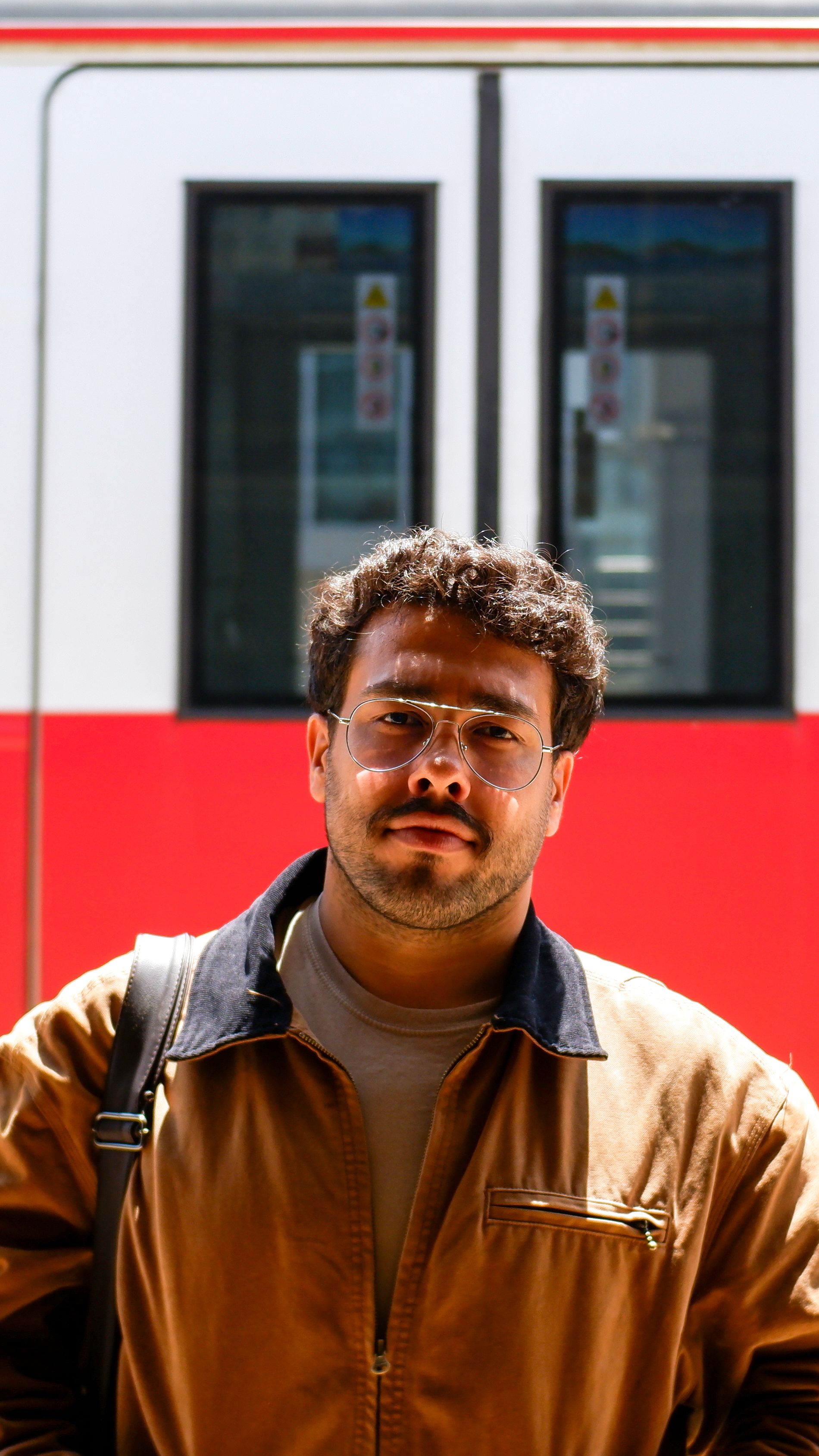 Portrait of a man with curly hair and mustache standing at a railway station.