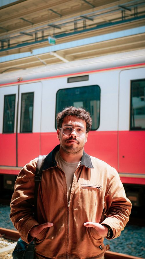 Free A fashionable man with glasses stands confidently at a railway station, hands in pockets. Stock Photo