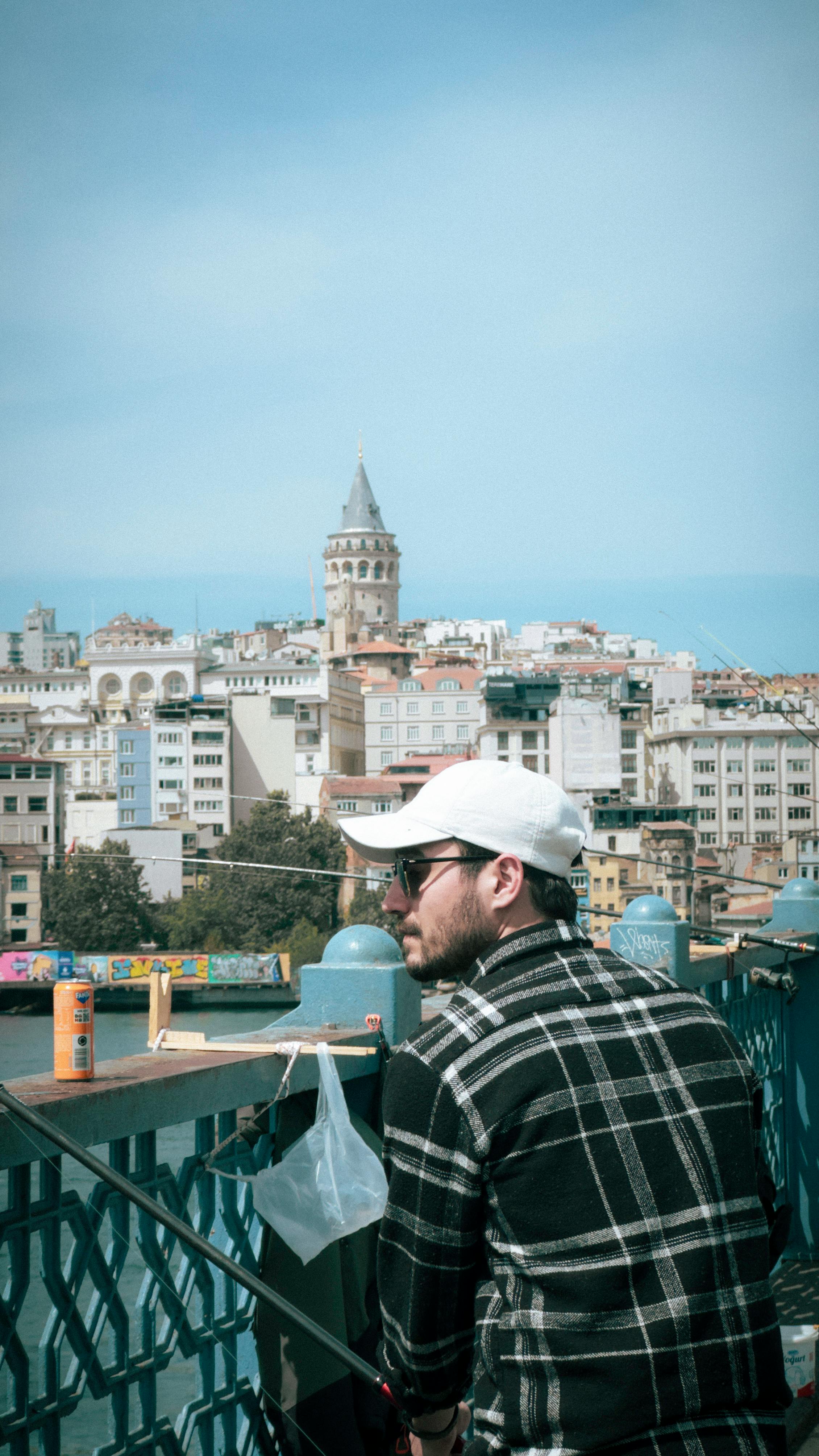 Man fishing with a view of Galata Tower in Istanbul, capturing urban lifestyle and leisure.