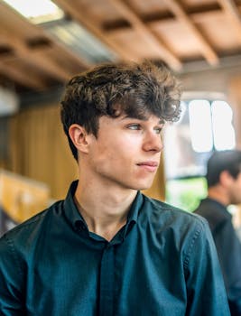 一个身穿黑色衬衫的年轻人若有所思地凝视着户外，透出沉思的感觉